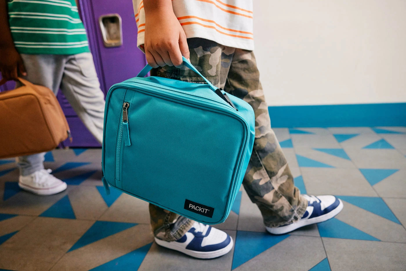 Child carrying a teal PackIt lunch bag at school